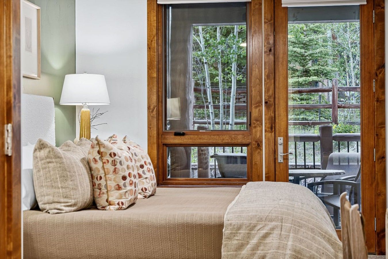 A bedroom with a bed, pillows, a lamp, and a window overlooking a deck.