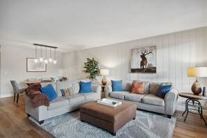 A modern living room with a grey sofa set, a brown ottoman, a dining table with chairs, and a large wall-mounted picture of a deer. - 5 minutes from Keystone Resort with Hot Tub & Pool (Keystone)
