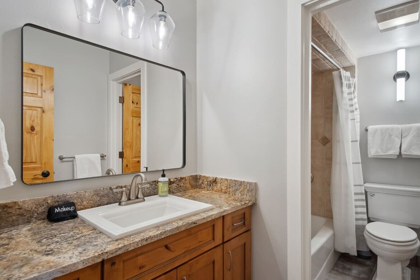 A bathroom with a white sink, wooden vanity, a large mirror, and a shower area.