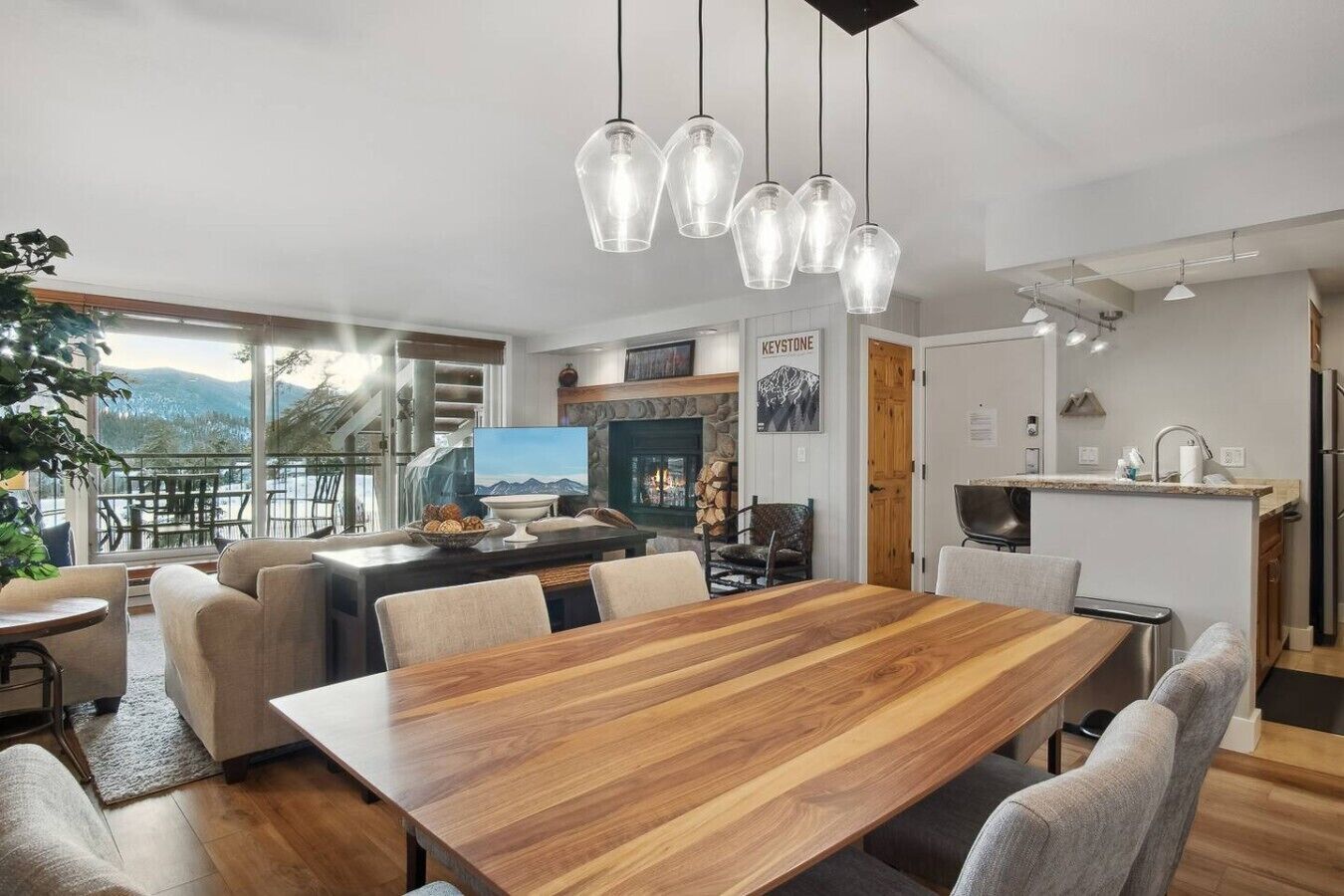 Een moderne keuken met een stenen open haard, een eethoek met een houten tafel en uitzicht op bergen door grote ramen.