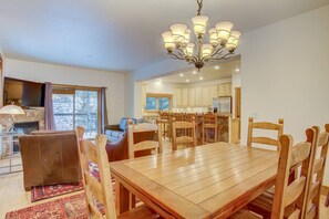 A spacious dining area with a wooden table and chairs, a chandelier, and a view of the kitchen in the background. - Private Hot Tub on Creek- 5 min to Gondola/Main St (Breckenridge)