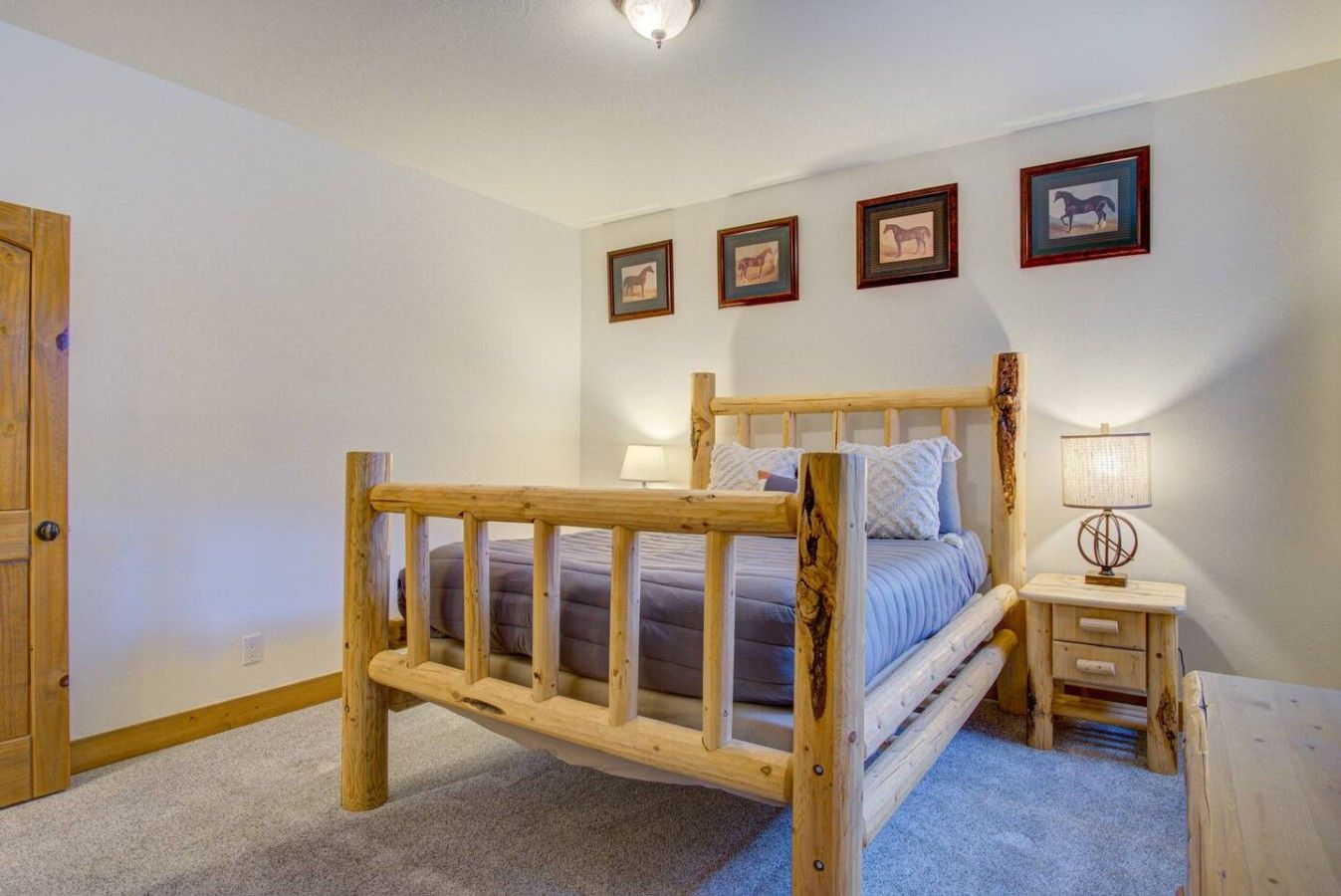 A bedroom with a wooden bed frame, a bedside table with a lamp, and framed pictures on the wall.