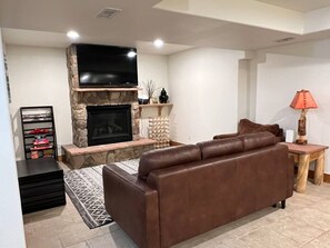 Ein Wohnzimmer mit Kamin aus Stein, einem braunen Ledersofa und einem Fernseher, der über dem Kamin angebracht ist.