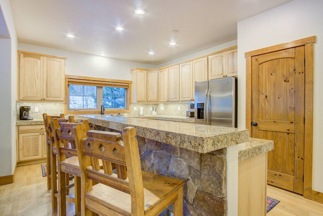 A kitchen with wooden cabinets, a stone island, and a stainless steel refrigerator.