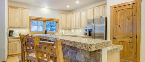 Una cocina con armarios de madera, una isla de piedra y un refrigerador de acero inoxidable.