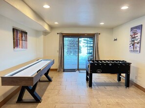 Ein Zimmer mit Billardtisch, Kicker und einem großen Fenster mit Vorhängen.