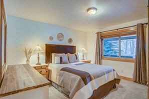 A bedroom with a large bed, two bedside tables, a nightstand, a window with curtains, and a view of trees. - Private Hot Tub on Creek- 5 min to Gondola/Main St (Breckenridge)