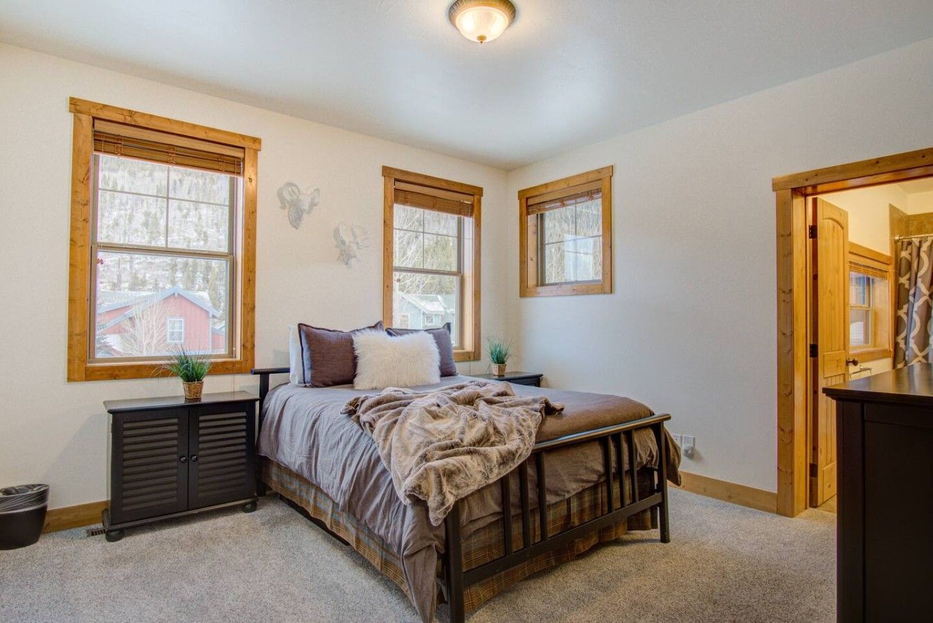 Une chambre à coucher comprenant un lit, deux tables de chevet, une commode et trois fenêtres.