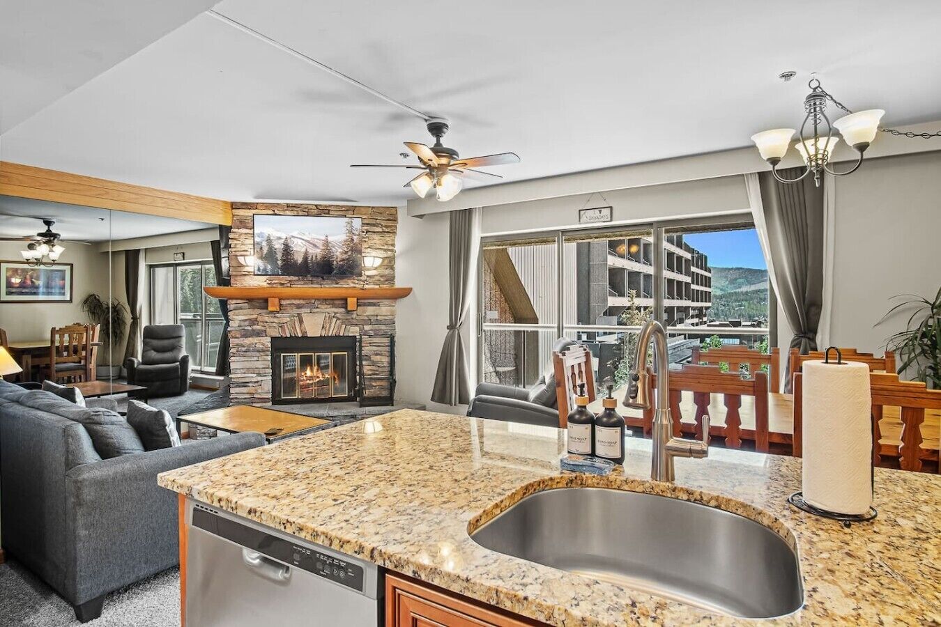 A modern living room with a fireplace, a dining area, and a kitchen with a granite countertop and stainless steel sink.