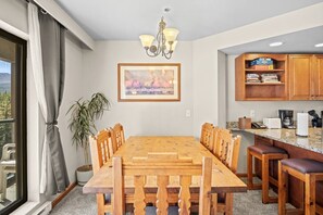 A dining area with a wooden table and chairs, a chandelier, a framed picture on the wall, and a view of the outdoors through a window. - 1 Bedroom True Ski-in/out in Beaver Run Building 4 (Breckenridge)