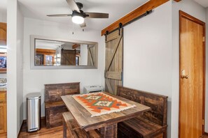 Ein Essbereich mit Holztisch und Bänken, Deckenventilator, einer Schiebetür im Bauernhausstil und einem Spiegel an der Wand.