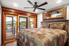 Een slaapkamer met een groot bed, een plafondventilator, een houten hoofdeinde en uitzicht door een schuifdeur.