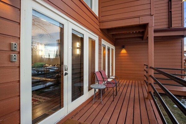 Una terraza de madera con puerta de vidrio, mobiliario exterior y barandilla.
