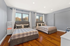 Une chambre moderne avec deux lits, une table de chevet, une commode et une fenêtre avec des rideaux.