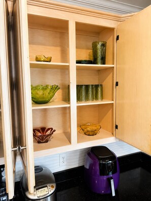 A kitchen with a wooden cabinet containing various glass bowls and a purple coffee maker on the counter. - Jamestown 4BR Estate (Jamestown)