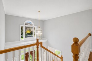 A staircase with white balusters and wooden handrails leading to a landing with a view of a green landscape. - Jamestown 4BR Estate (Jamestown)