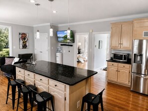 A modern kitchen with a large island, stainless steel appliances, and a flat-screen TV mounted above the island. - Jamestown 4BR Estate (Jamestown)