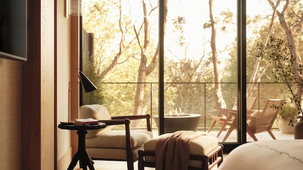 A room with a large window, a bed, a chair, a table, and a plant.