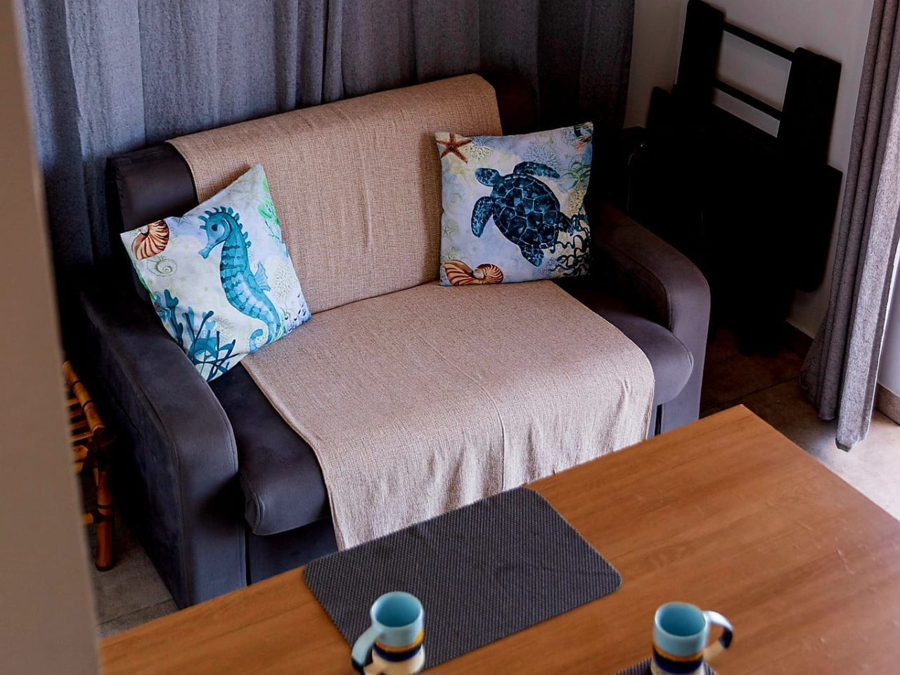 A cozy seating area with a sofa, two pillows with sea turtle designs, a blanket, and a wooden table with two cups.