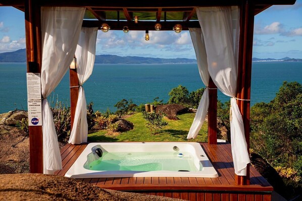 A wooden deck with a hot tub and a view of the ocean.