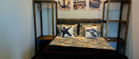 A bedroom with a bed, floral bedding, and three wall-mounted paintings.