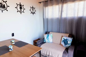Una habitación con un sofá, una mesa con dos tazas y adornos en la pared, incluyendo un barco y un caballito de mar.