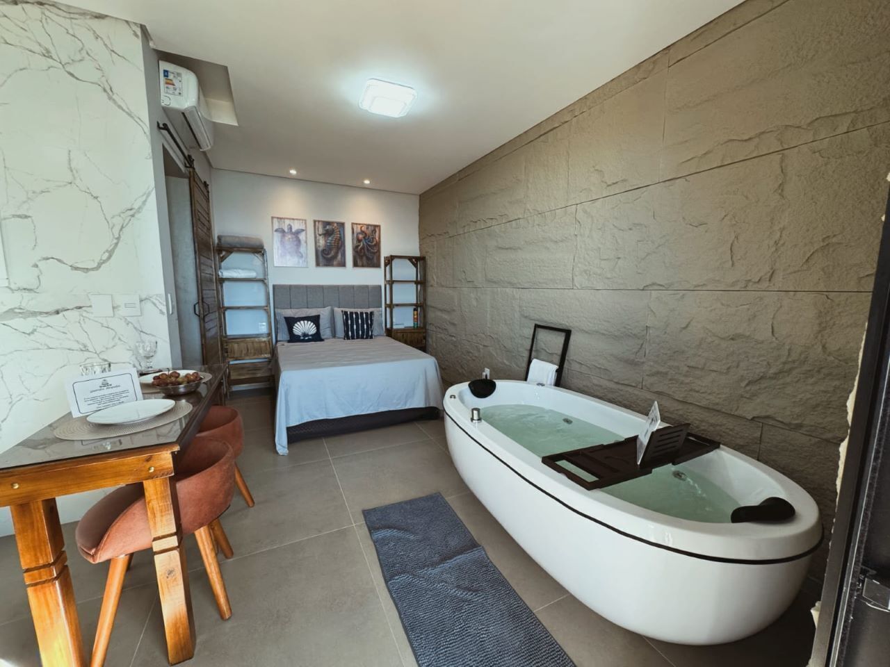 A modern bedroom with a large bathtub, a dining table with chairs, and a bed with a headboard.