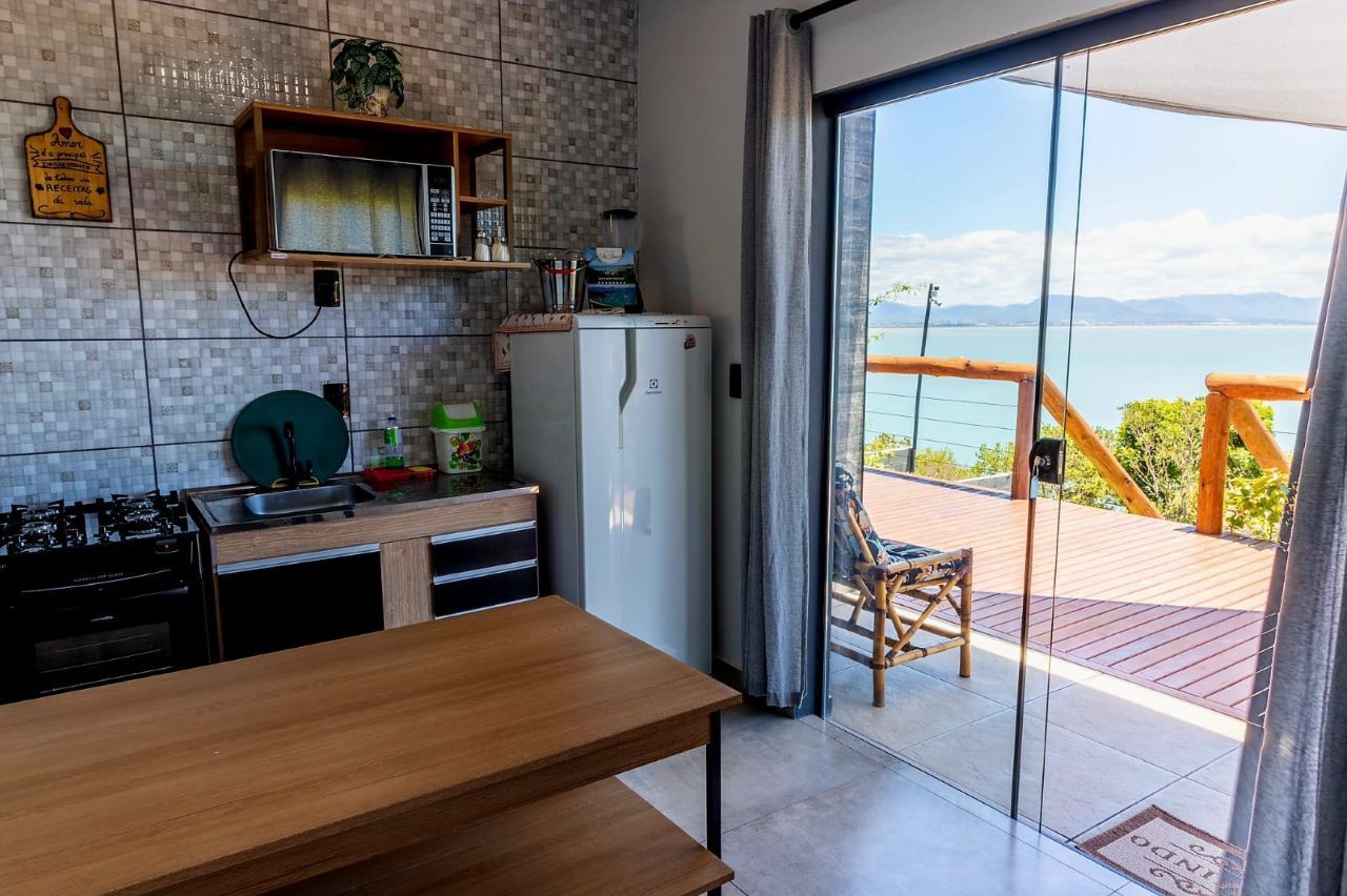 Una cocina con una mesa de madera, un refrigerador y vista al mar a través de un ventanal corredera.