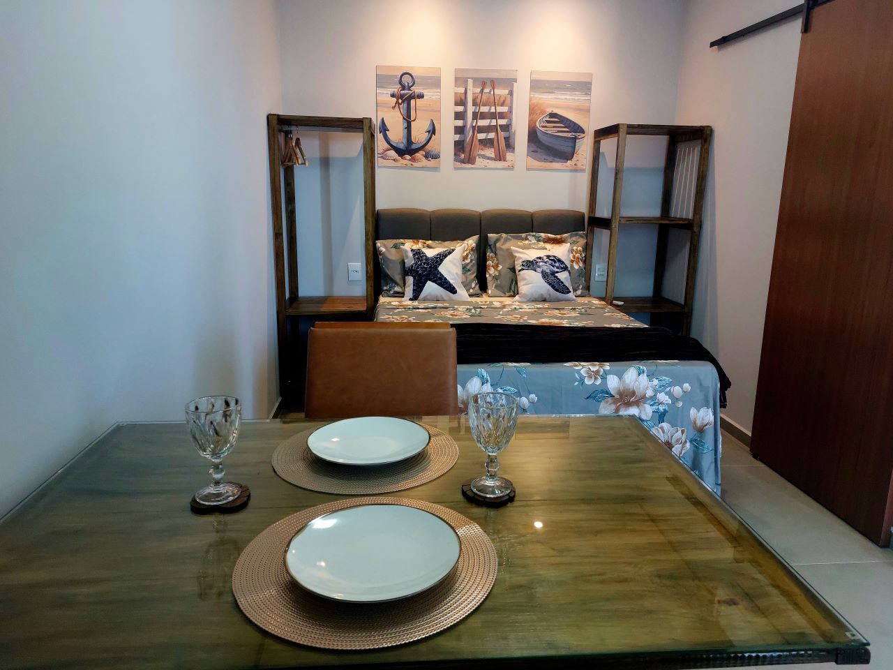 Uma área de refeições com uma mesa de vidro, dois pratos e dois copos de vinho.