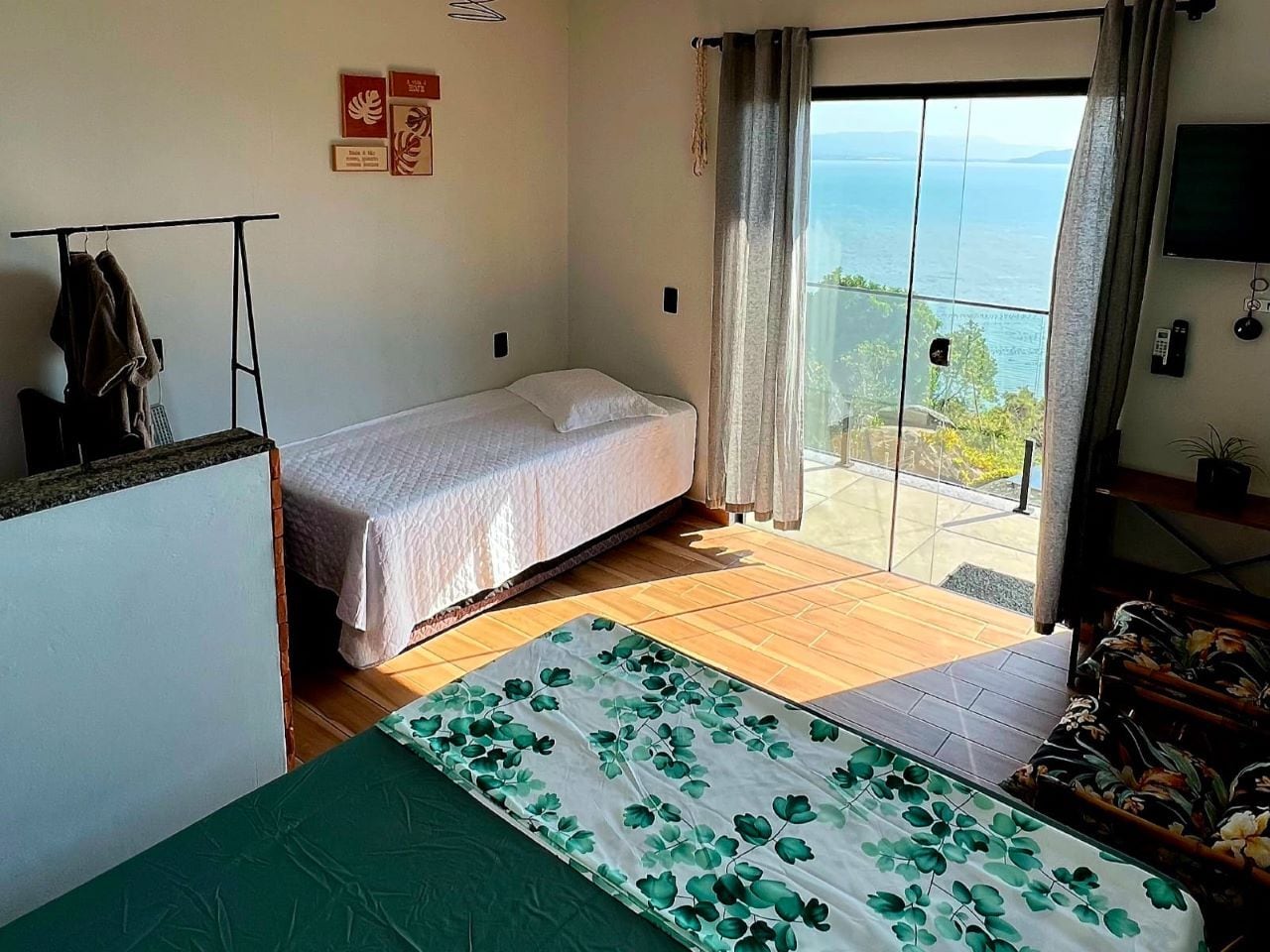 Quarto com cama, uma mesa pequena, cadeira e vista para o mar, além de uma TV na parede.