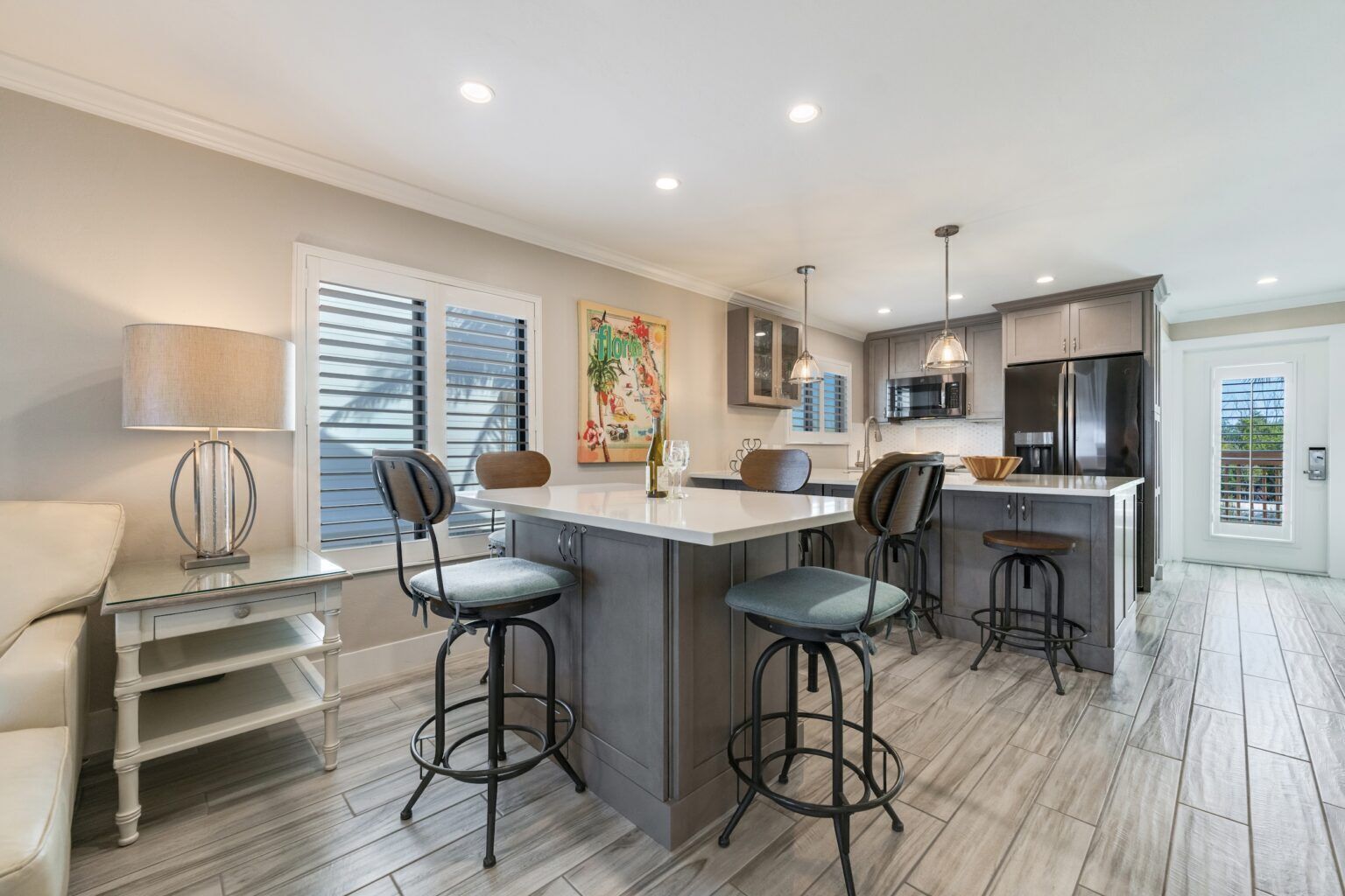 A modern kitchen with a central island, bar stools, a dining table, and a sofa.
