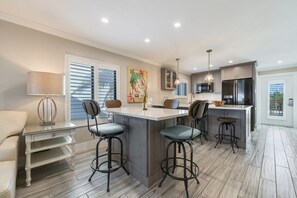 Una cocina moderna con una isla central, taburetes de bar, una mesa de comedor y un sofá.