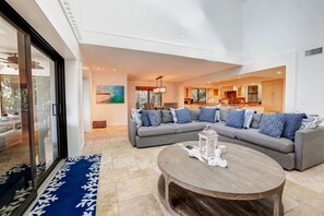 A modern living room with a sectional sofa, a round coffee table, and a view into the kitchen. - Captiva Home w/ Private Pool & Gulf Views (Captiva)