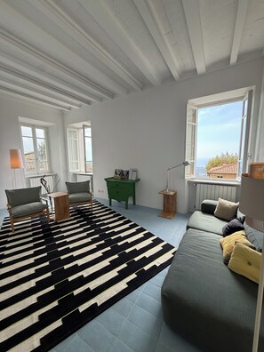 A spacious living room with a black and white striped rug, a green sofa, and a view of the outdoors through a large window. - Stylish, high-end villa in the hills of Versilia with ocean views (Toscana)