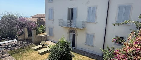 A two-story building with a stone patio, a small garden, and a balcony.