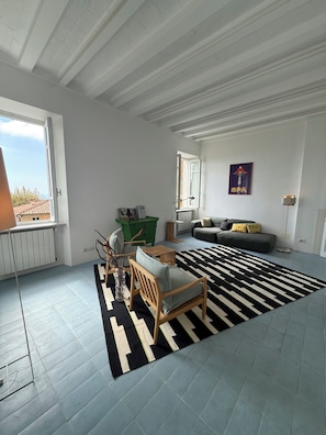 A spacious living area with a sofa, a wooden chair, a patterned rug, and a radiator. - Stylish, high-end villa in the hills of Versilia with ocean views (Toscana)