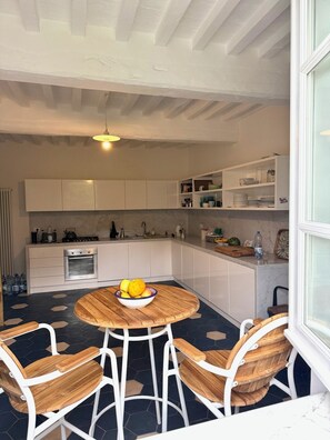 A kitchen with a round wooden table, white chairs, and a bowl of fruit. - Stylish, high-end villa in the hills of Versilia with ocean views (Toscana)