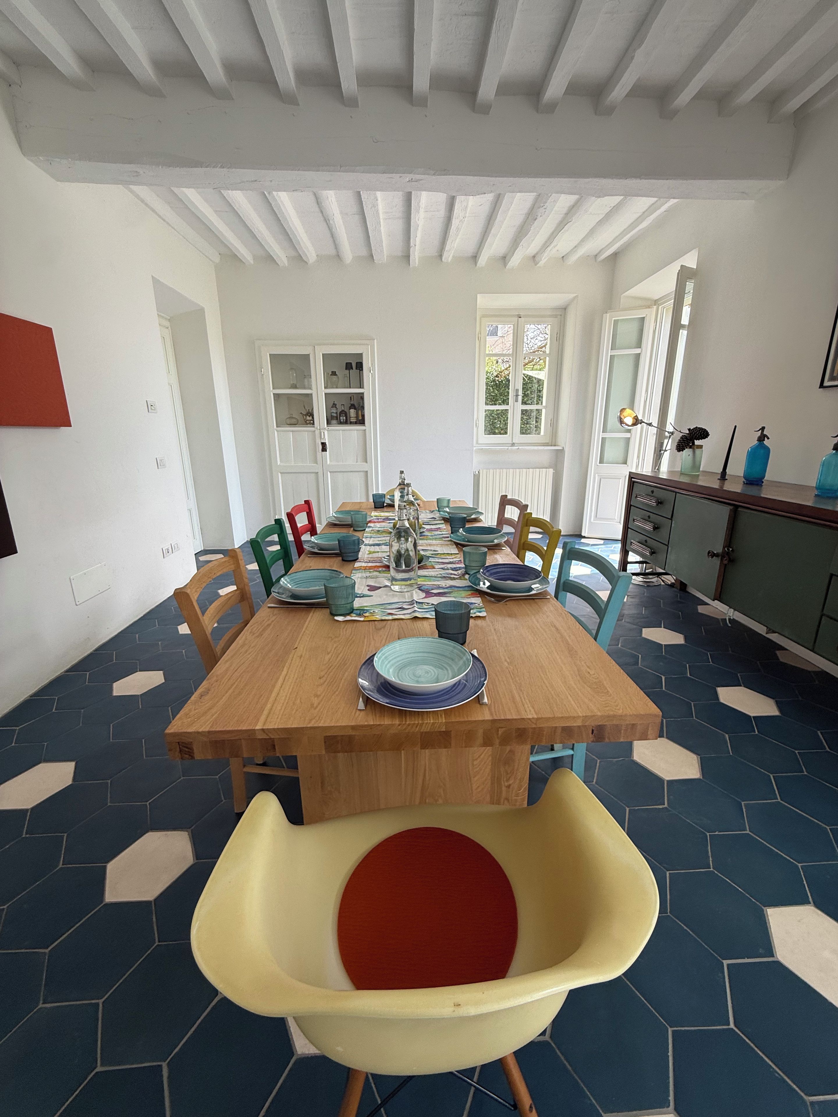 A dining area with a wooden table set for four, surrounded by chairs with colorful cushions.