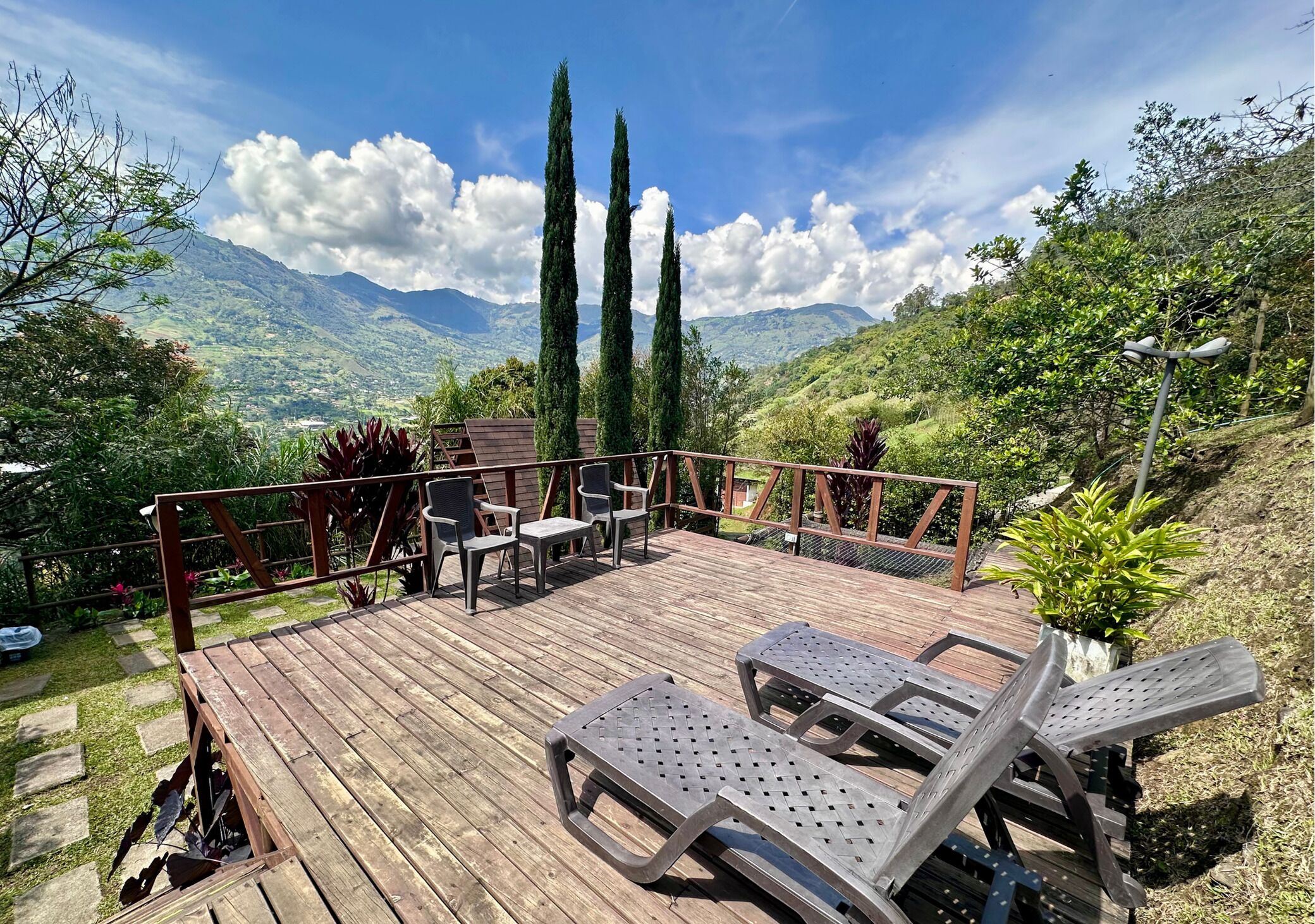A wooden deck with lounge chairs and a table, overlooking a mountainous landscape.