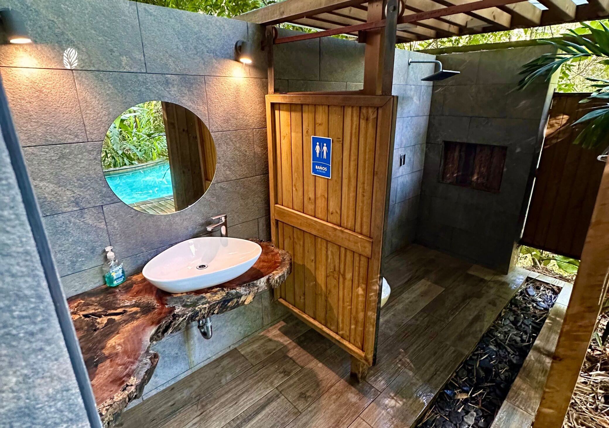 A bathroom with a wooden shower enclosure, a sink with a marble countertop, and a round mirror.