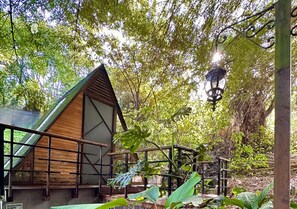Una cabaña de madera con techo inclinado, rodeada de exuberante follaje y un farol colgante.
