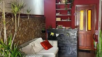 Um quarto aconchegante com sofá, parede de pedra decorativa, porta de madeira e uma estante com diversos objetos.