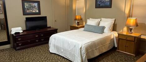 Une chambre d’hôtel comprenant un lit, une commode, un téléviseur, un ventilateur de plafond et deux lampes.