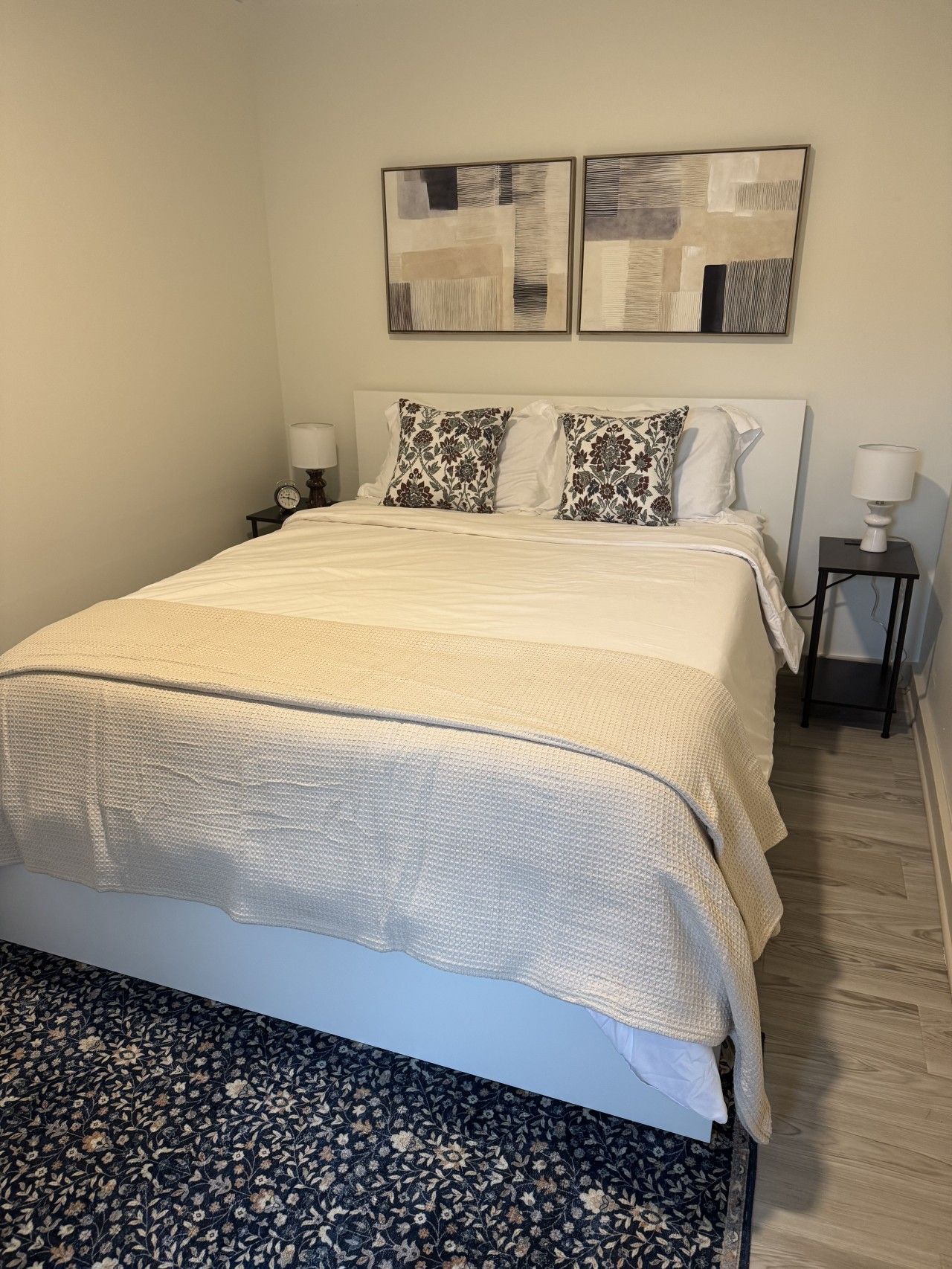 Een slaapkamer met een groot bed, twee nachtkastjes, een wandlamp en twee abstracte schilderijen aan de muur.