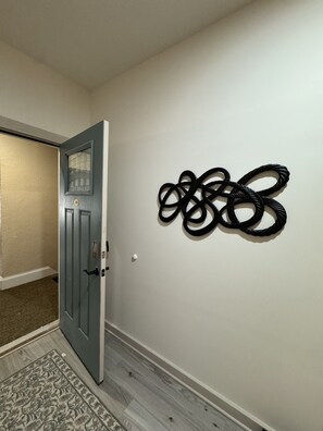 A hallway with a closed door, a patterned rug, and a wall-mounted abstract sculpture. - 205 Bright Studio near Hospitals and Downtown (Indianapolis)