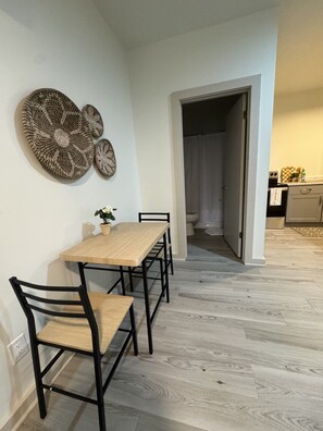 Een eethoek met een tafel, stoelen, een potplant en decoratieve wanddecoratie.