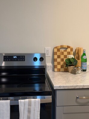 A kitchen with a stove, oven, and a countertop with a cutting board, a bottle, and a plant. - 205 Bright Studio near Hospitals and Downtown (Indianapolis)