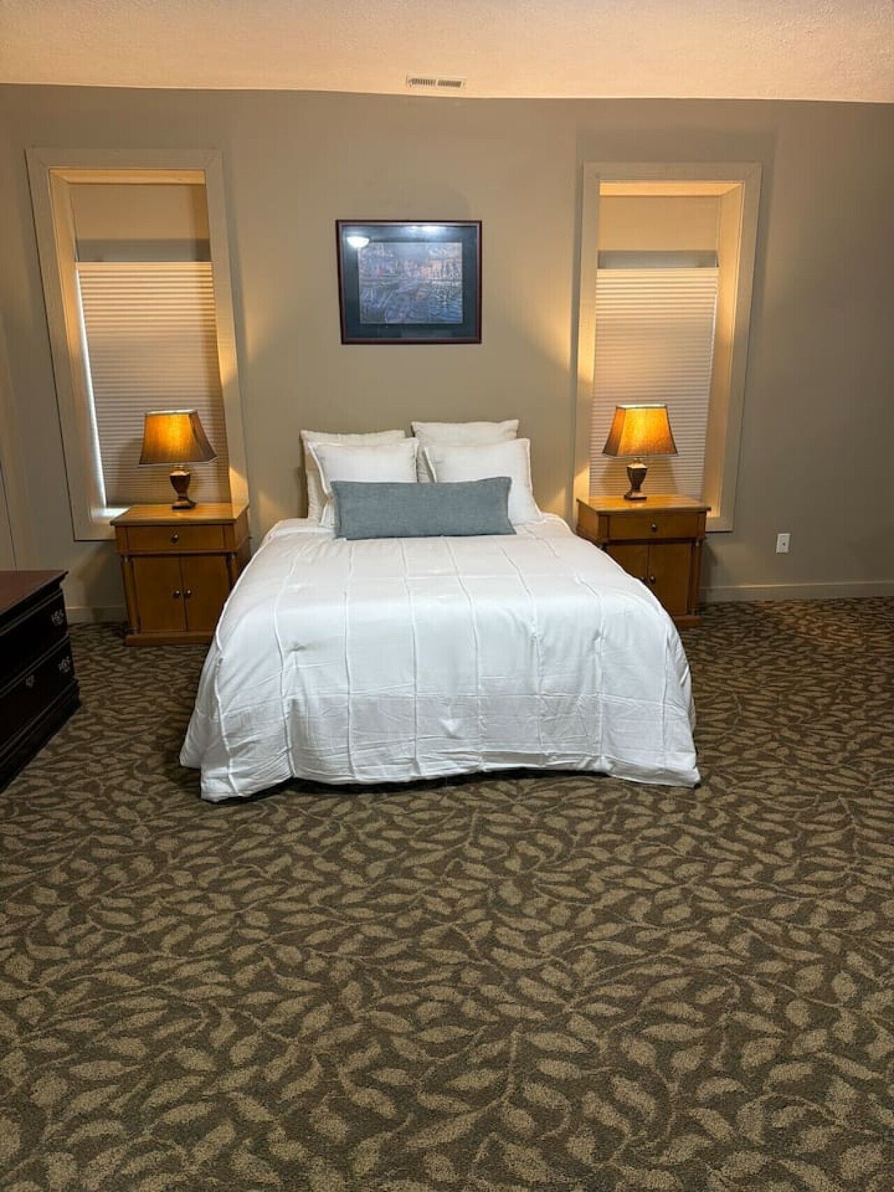 Een hotelkamer met een groot bed, twee nachtkastjes, een ingelijste foto aan de muur en een kamerbreed tapijt met dessin.