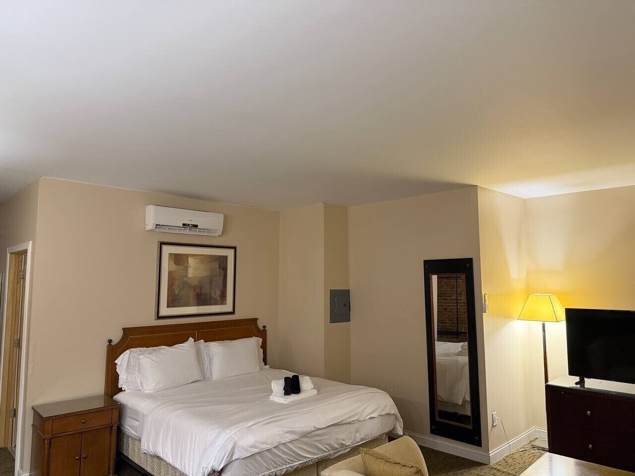 Een hotelkamer met een bed, nachtkastje, lamp, televisie en een spiegel.
