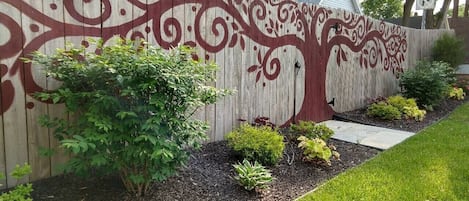 Une clôture en bois ornée de motifs d’arbres, un chemin et des parterres de fleurs aménagés.